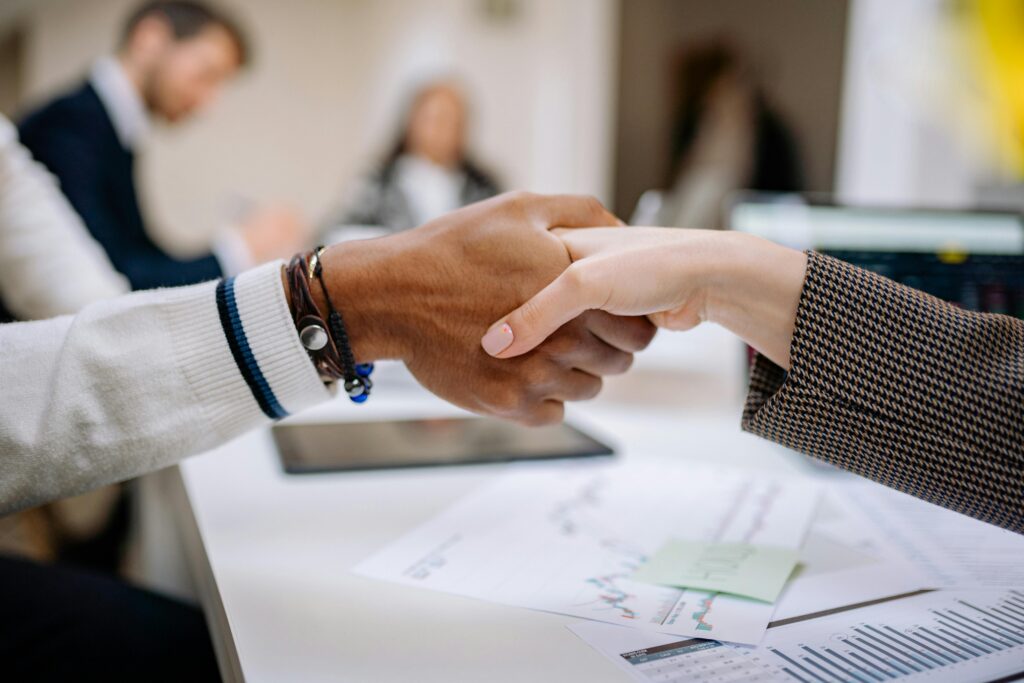 Two small business owners shaking hands over a business deal with financial documents on the table