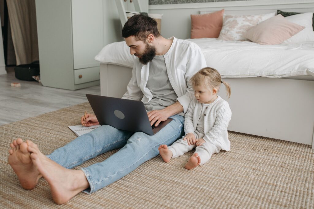 Father with laptop and daughter in bedroom demonstrating remote work life balance